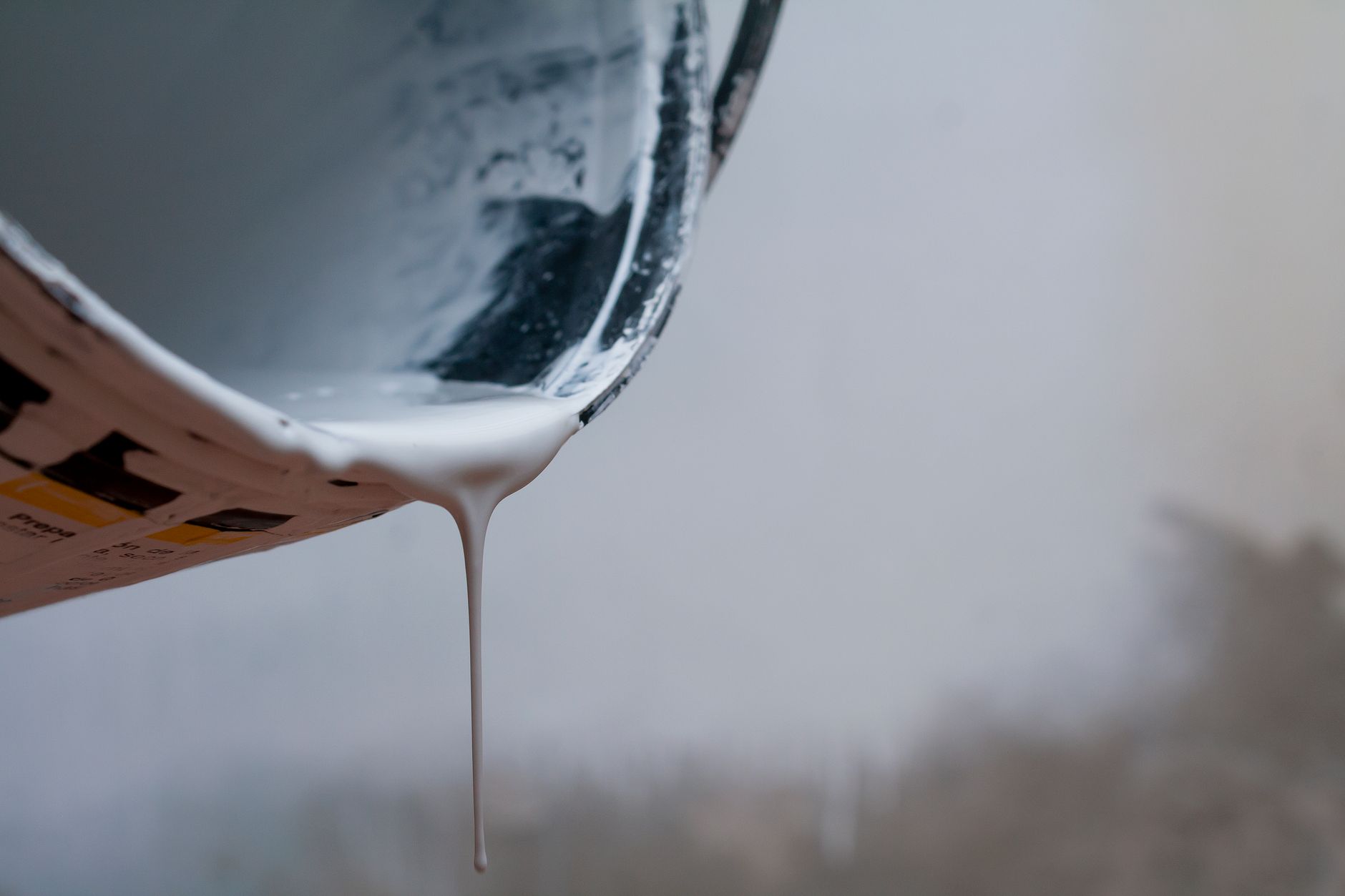 Close-up of white paint pouring from a bucket, showcasing texture and fluidity in Carlsbad, CA